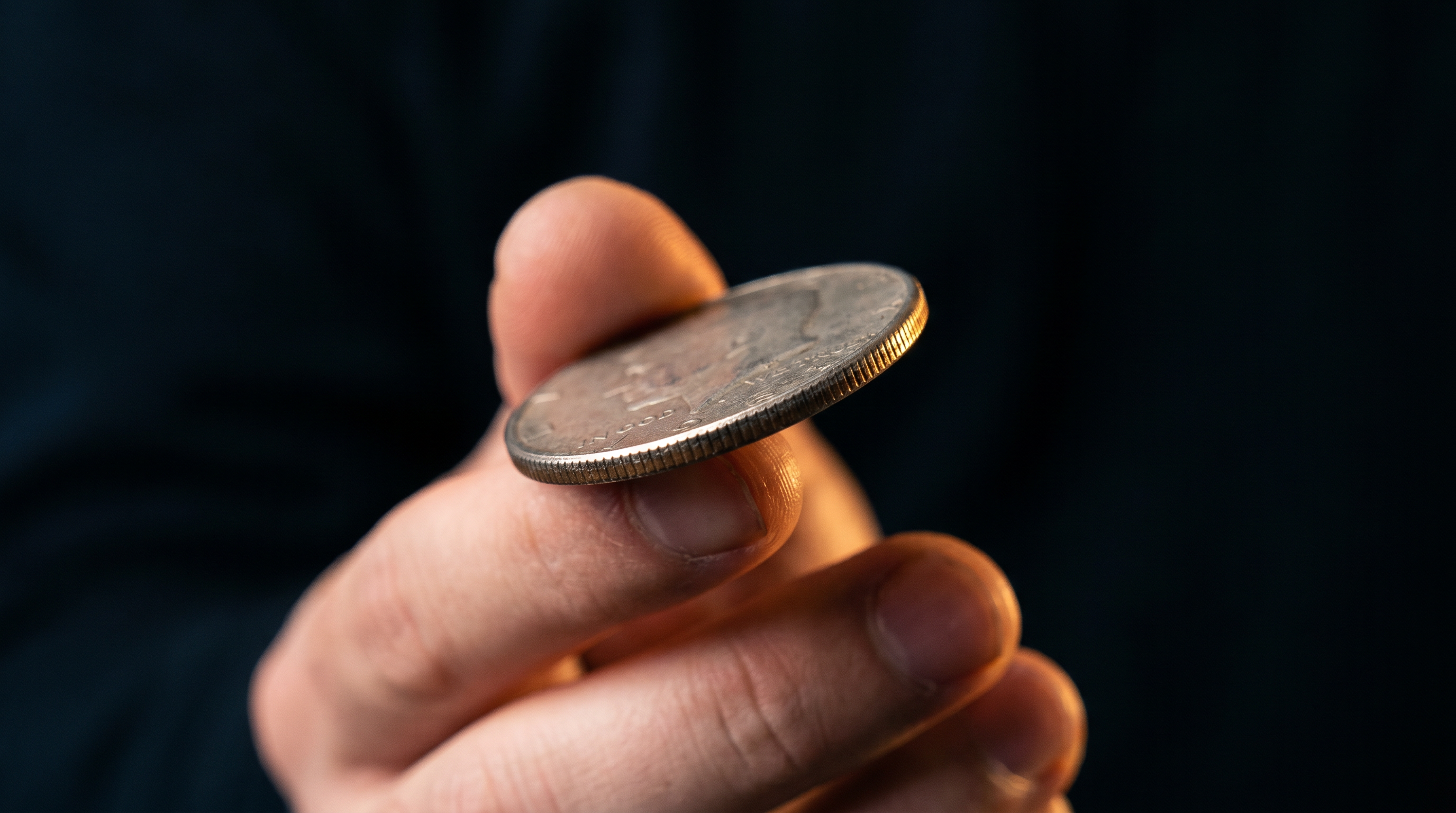 A half-dollar coin balanced in fingertips, mid-gesture in a sleight-of-hand trick.