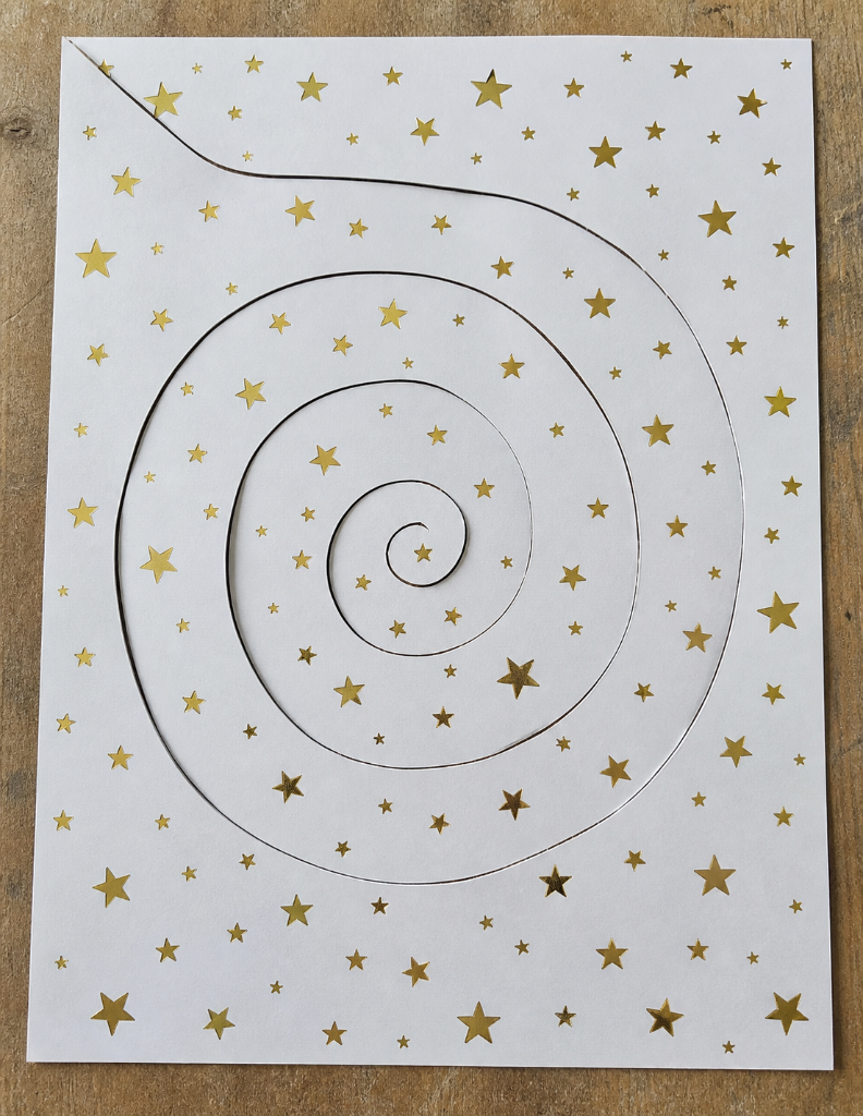 Flat paper with gold stars and a spiral cut traced across it — before lifting